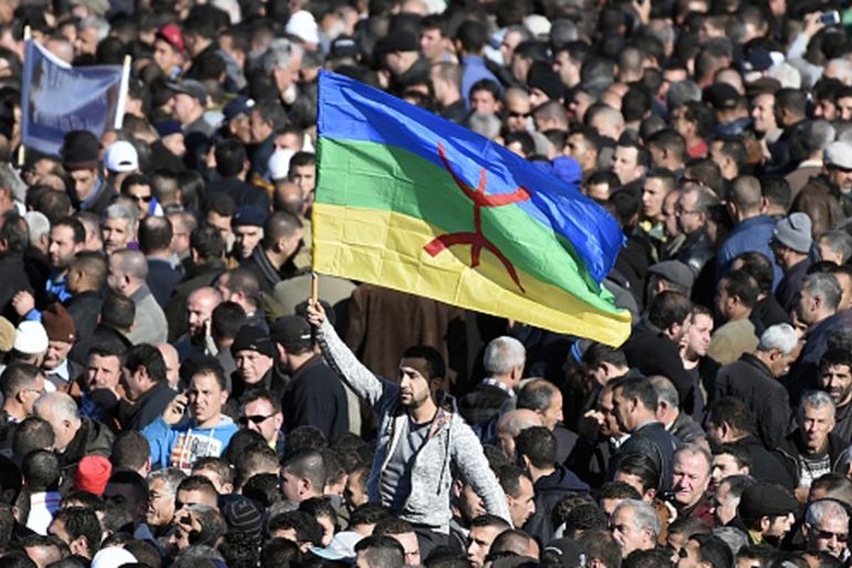 A man waves the Amazigh flag as thousands of mourners attend the funeral procession and burial of one of the fathers of Algeria''s struggle for independence [AFP]
