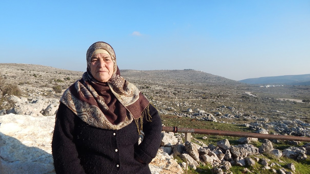 
'I want to pass on my land to my 30 children and grandchildren, who have a right to it,' said Mariam, with the Amona outpost, built on her land, in the distance behind her [Shatha Hammad/ Al Jazeera]
