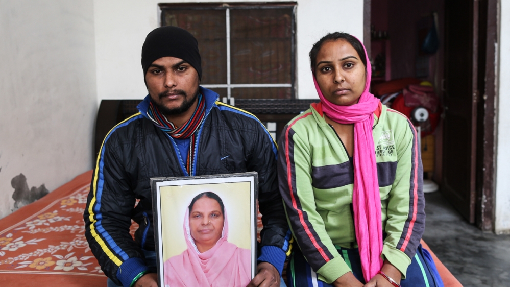 Parminder Singh holds a picture of his 50-year-old mother who died while waiting in a queue at an ATM. His sister, right, blames herself as their mother was trying to withdraw money to pay for her wedding [Showkat Shafi/Al Jazeera]
