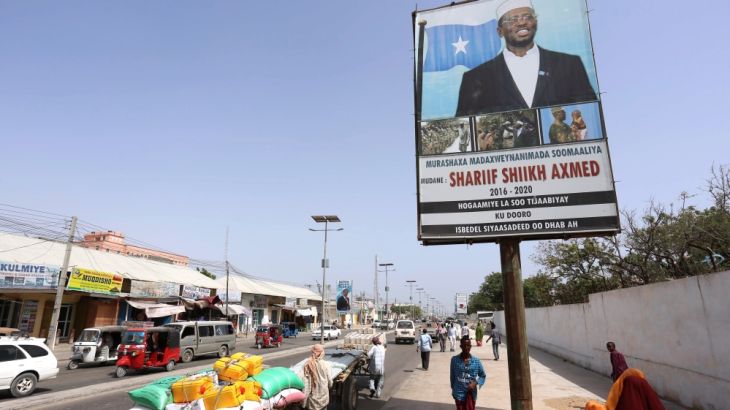 People walk along a street with the campaign billboard of Somalia''s Presidential candidate Sharif Sheikh Ahmed in Somalia''s capital Mogadishu