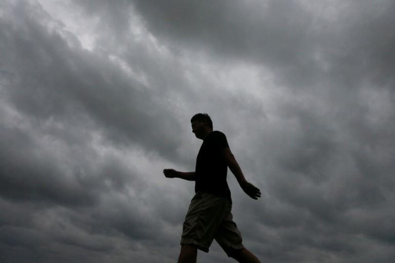 A man walks along a road as storm clouds gather above him in Colombo