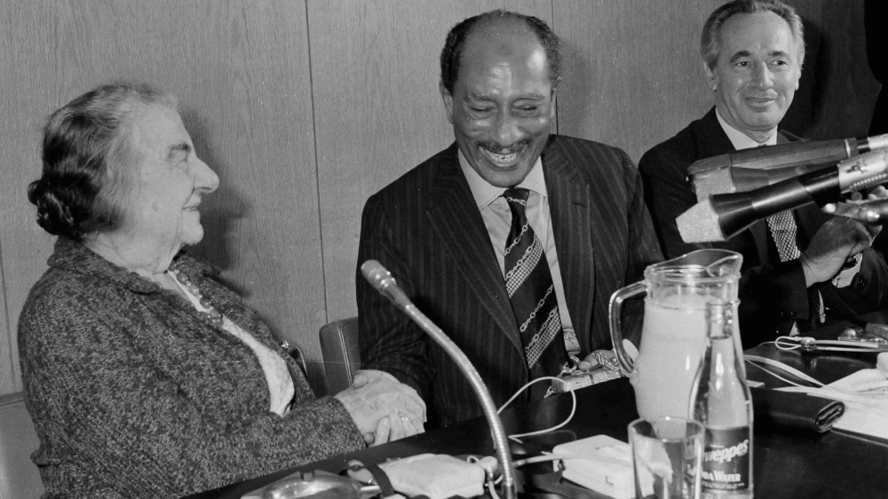 Egyptian President Anwar Sadat shakes hands with former Israeli Prime Minister Golda Meir, attended by Shimon Peres, the leader of the Israeli Labor Party, in the Knesset building, Jerusalem on November 21, 1977 [File: AP]