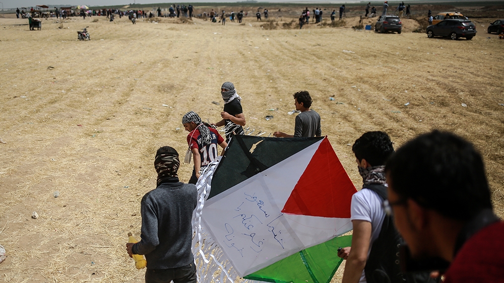 Palestinians fly a kite with the words: 'We will return despite the betrayers' [Hosam Salem/Al Jazeera]