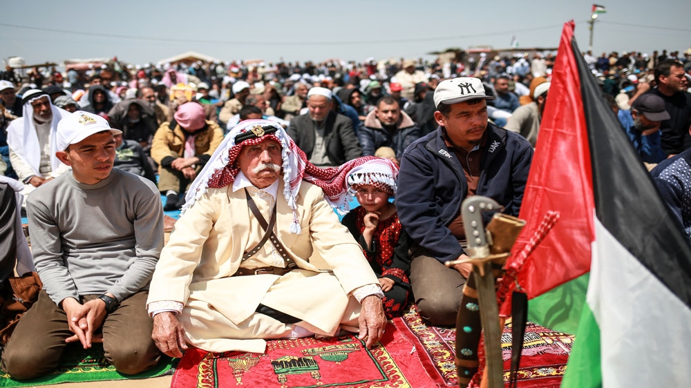 An elderly Palestinian man and his granddaughter sit during Friday prayers at at one of the encampments east of Khuza'a in the southern Gaza Strip [Hosam Salem/Al Jazeera] 
