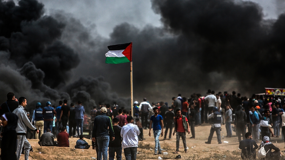 Palestinians raise their flag in front of burning tyres they lit near the border with Israel, east of Gaza City [Hosam Salem/Al Jazeera]