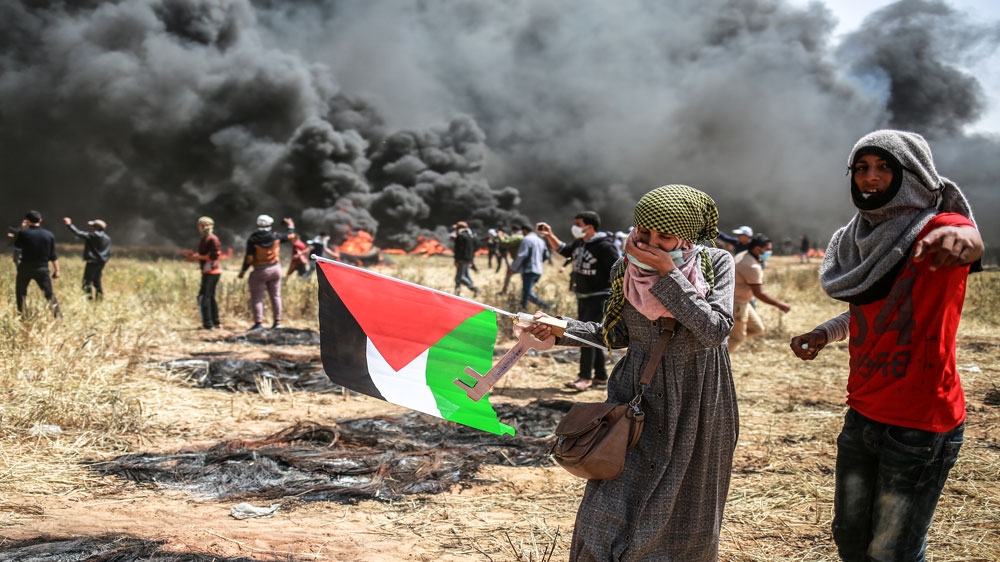 A Palestinian woman and man stand behind burning tyres in Khuza'a near the border in southern Gaza Strip [Hosam Salem/Al Jazeera] 