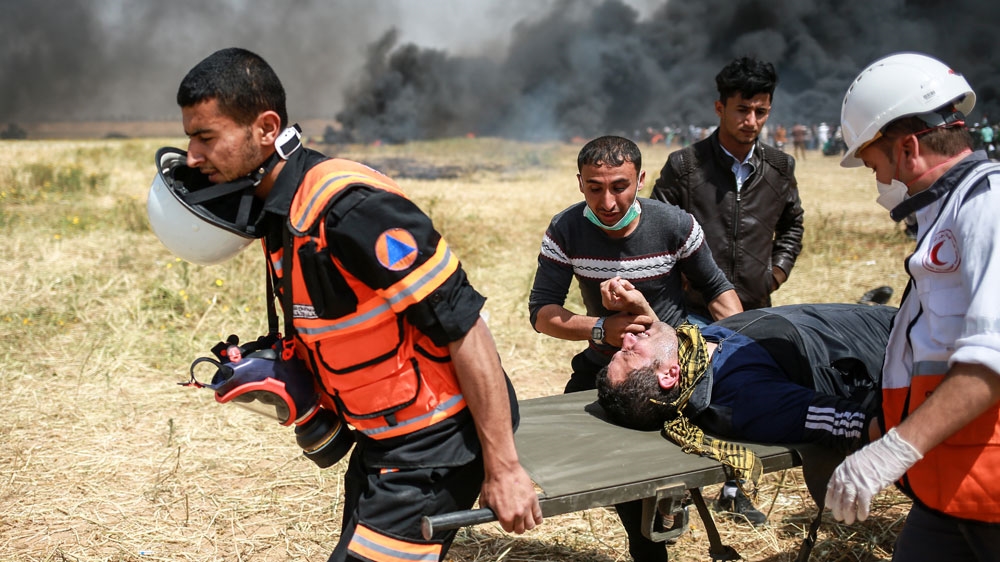 Medics carry a wounded protester on a stretcher in Khuza'a, Khan Younis, on the third consecutive Friday protest near the Gaza Strip border [Hosam Salem/Al Jazeera] 