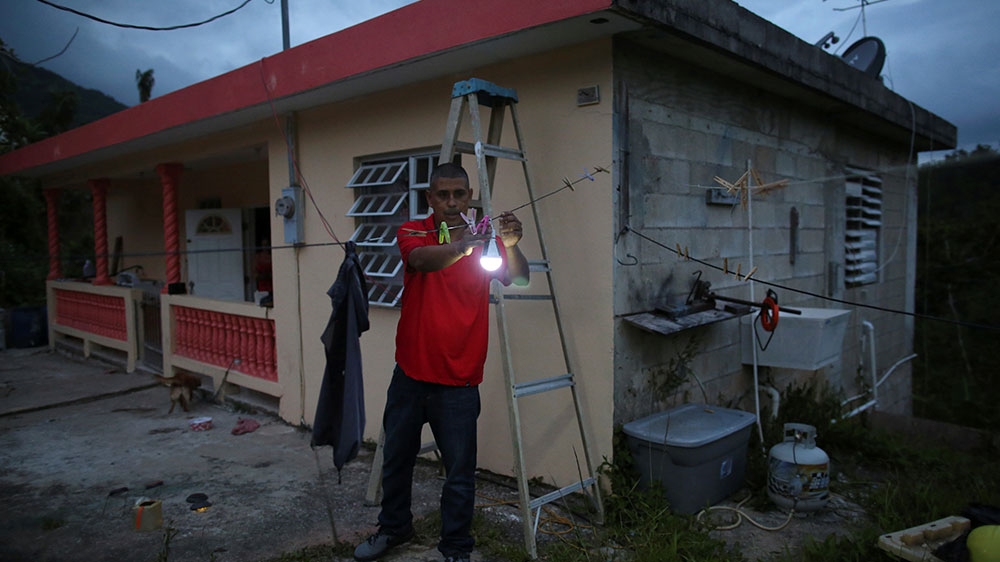 Wilson Reyes attaches a solar lamp to a clothesline outside his home, as his neighbourhood was still without power nine months after Hurricanes Irma and Maria battered the island [File: Alvin Baez/Reuters] 