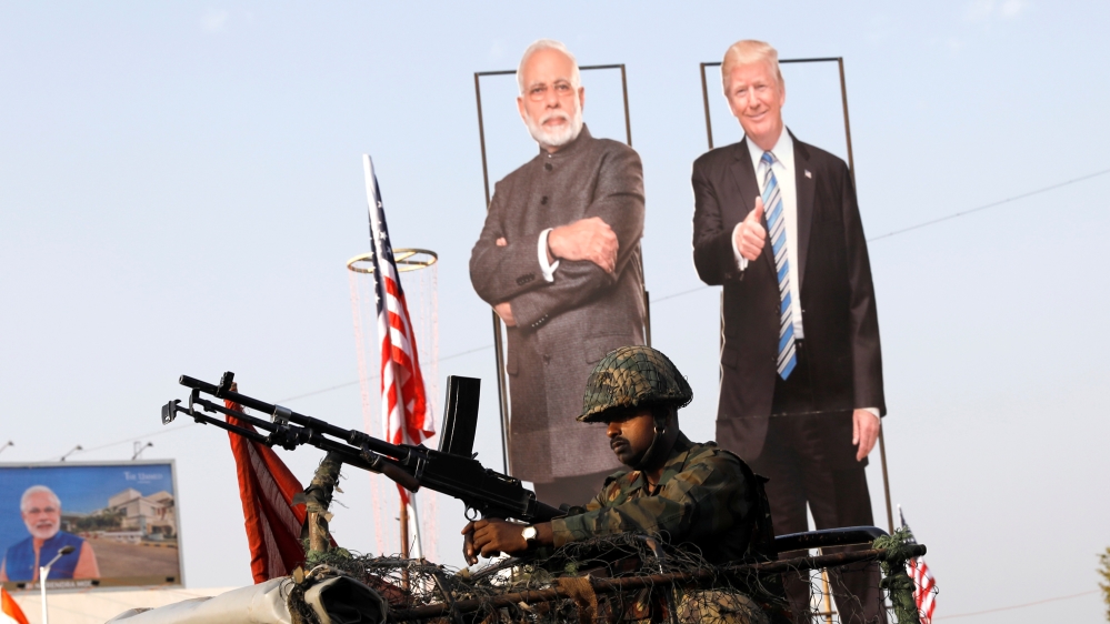 An Indian army soldier sits atop an armoured vehicle next to cutouts of India's Prime Minister Narendra Modi and U.S. President Donald Trump along a road, ahead of Trump's visit, in Ahmedabad
