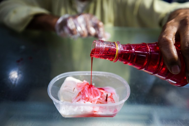 PHoto of a man's hand drizzling rooh afza onto a bowl of falooda
