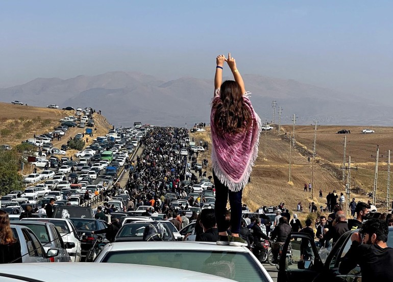 An unveiled woman standing on top of a vehicle as thousands make their way towards Aichi cemetery in Saqez, Mahsa Amini's home