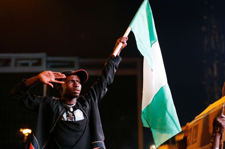 A demonstrator salutes as he raises the Nigerian flag during a protest over alleged police brutality