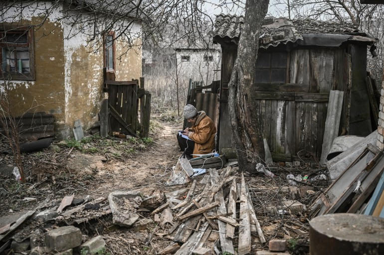 A woman keeps notes and uses her smartphone as she sits in house yard in the town of Chasiv Yar, near Bakhmut, Ukraine.