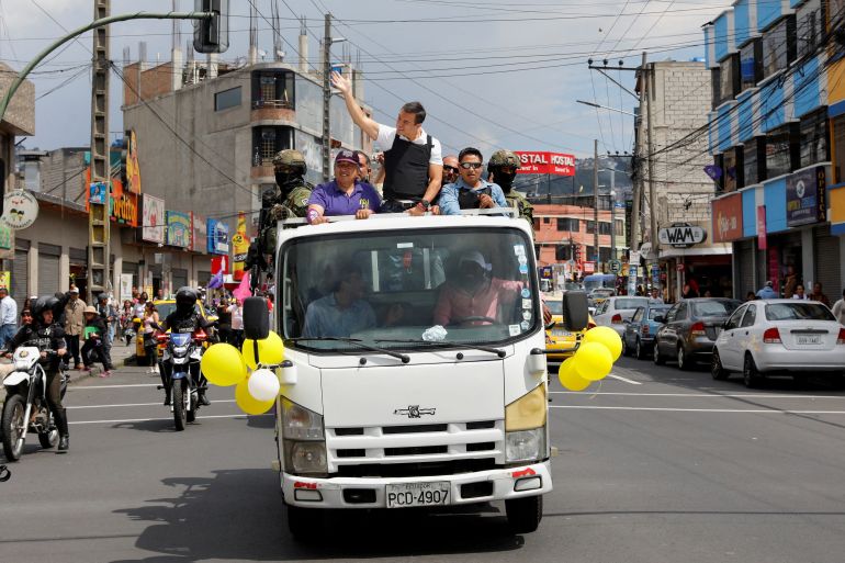 Daniel Noboa rides on the back of a truck, standing up against its cab and waving to supporters on the side of the road in Quito, Ecuador.