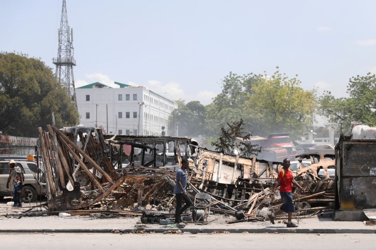 People walk past remains of vehicles near the presidential palace, after they were set on fire by gangs, as violence spreads and armed gangs expand their control over the capital, in Port-au-Prince, Haiti