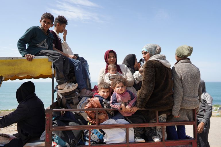 Women and children sitting in an open trailer as they travel to the south of Gaza. Some are sitting on the roof of the driver's cab