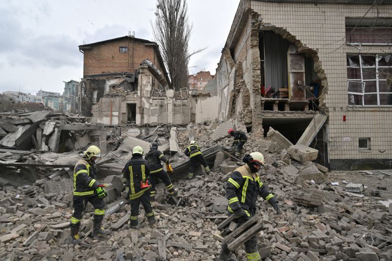 Rescue workers working at the site of a Russian missile attack in Kyiv. They are standing on rubble. There's a hole in the side of the building.