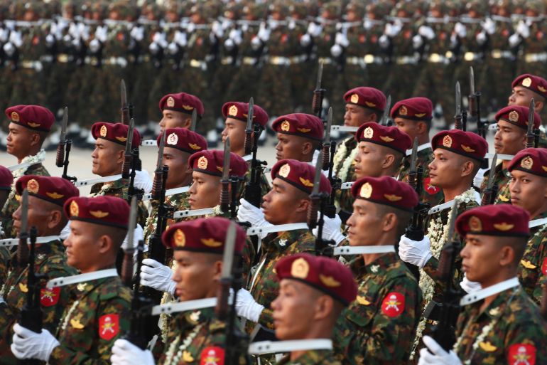 Myanmar military officers marching in formation for Armed Forces Day. They are wearing burgundy-coloured berets and are holding their weapons.