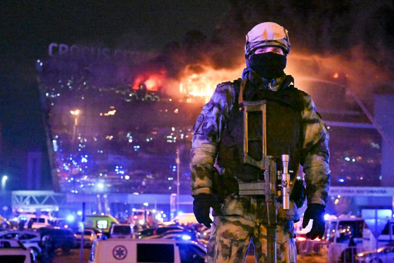 A member of Russia's national guard at the Crocus Concert Hall. The building is behind him in flames.