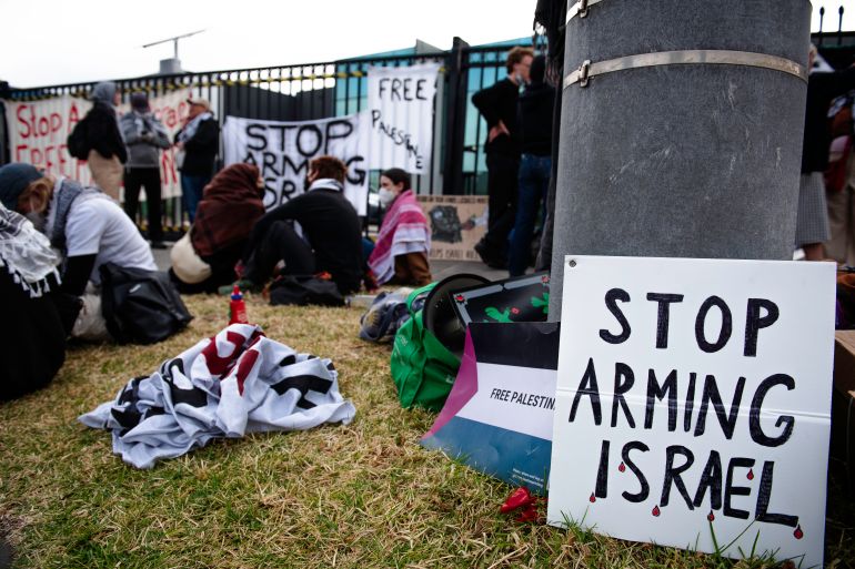Protesters sitting outside the HTA factory in the Melbourne suburbs,. There is a large placard reading 'Stop arming Israel"