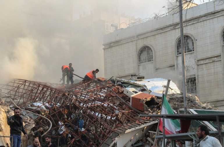Members of the civil defence stand near a damaged site after what Syrian and Iranian media described as an Israeli air strike on Iran's consulate in the Syrian capital Damascus