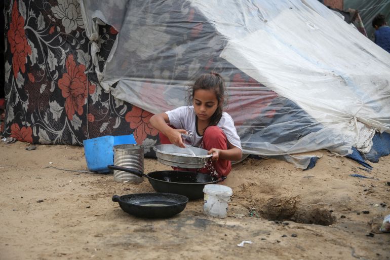 A girl pours water next to a tent, in Rafah