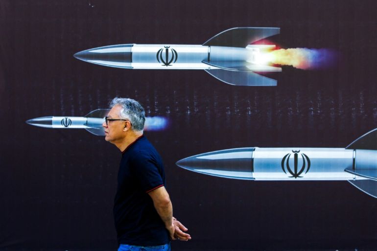 A man walks past a banner depicting missiles along a street in Tehran