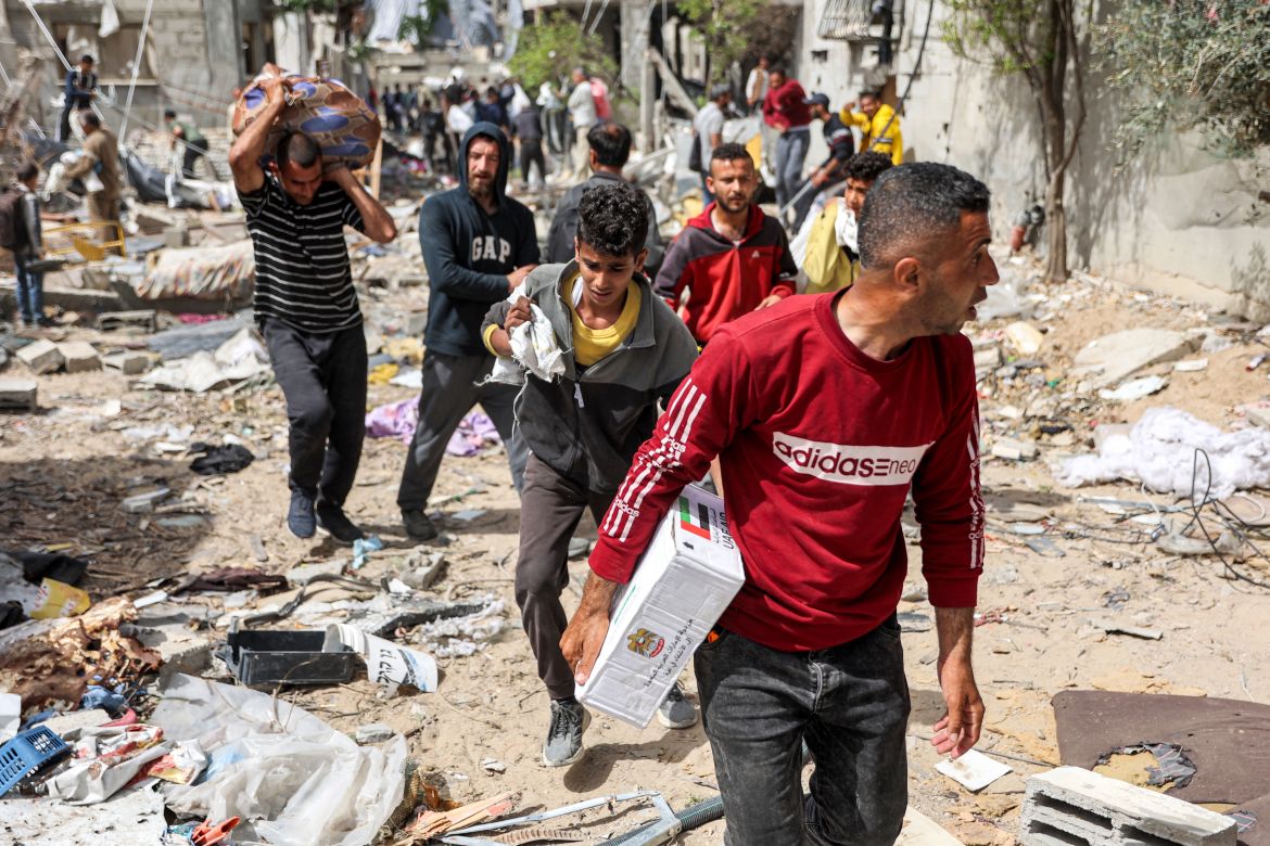 People walk through rubble past damaged buildings with humanitarian aid packages collected from a drop over the northern Gaza Strip