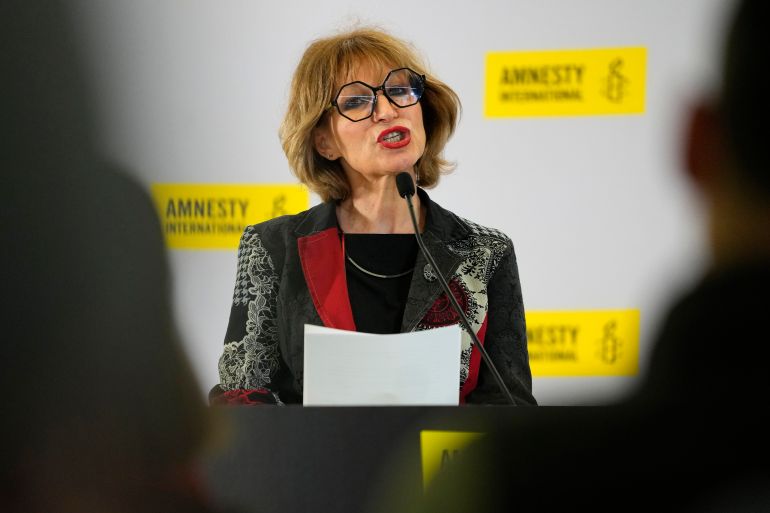gnes Callamard, Secretary General of Amnesty International. Callamard is speaking at a press conference. She has blonde hair and is wearing large black glasses.