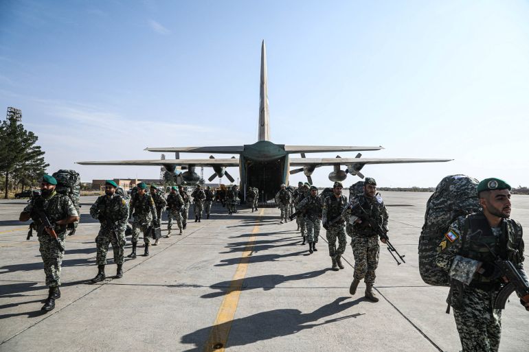 Iranian soldiers at a base in Isfahan. They are walking on a runway. There is a plane behind them.