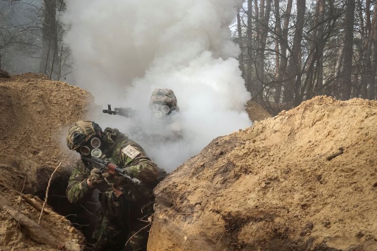Ukrainian soldiers wearing gas masks as they take part in radiation, chemical and biological hazard drills. They are moving through a trench., There is smoke