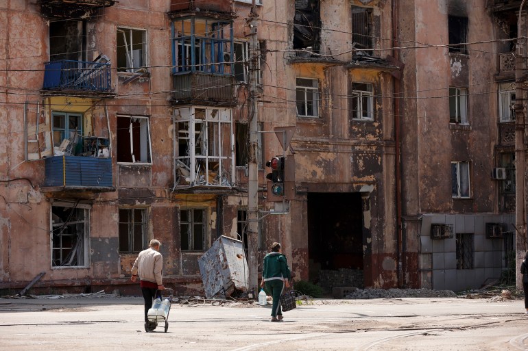 Locals walk amid destroyed buildings in Mariupol near the Illich Iron Steel Works Metallurgical Plant, Donetsk, eastern Ukraine, Friday, May 27, 2022