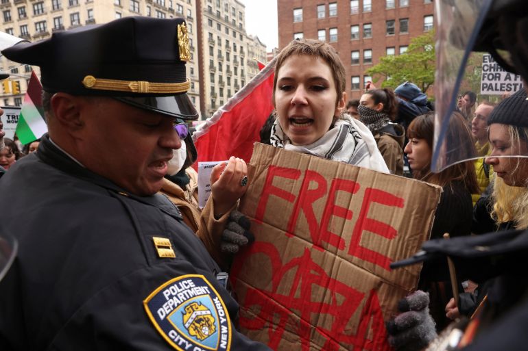 A demonstrator holds a placard near a police officer, during a protest in solidarity with Pro-Palestinian organizers on the Columbia University campus, amid the ongoing conflict between Israel and the Palestinian Islamist group Hamas, in New York City, U.S., April 18, 2024. REUTERS/Caitlin Ochs