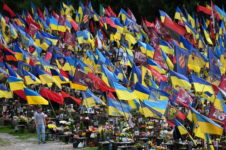 Flags, including the Ukrainian flag, displayed on graves at a cemetery in Lviv. A man is walking in front.