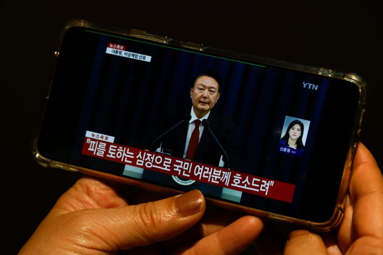 A South Korean tourist watches a Japanese TV broadcast on a phone showing Yoon declaring martial law in a televised emergency address